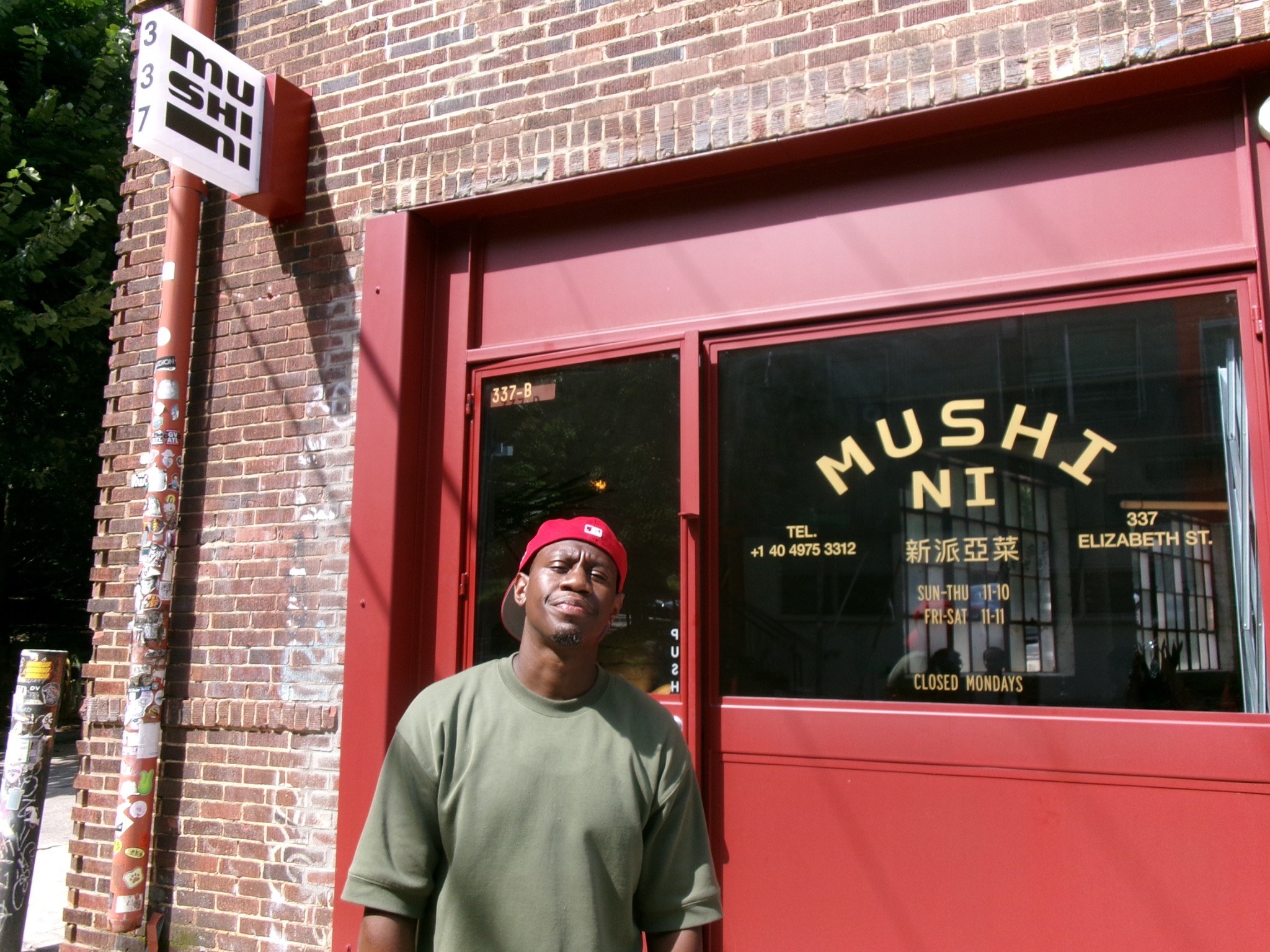 Ronny My standing outside a storefront in a red cap and green shirt